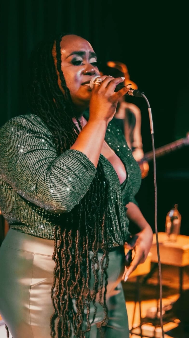 Doll McCoy singing into a microphone on stage, in a green sequined top