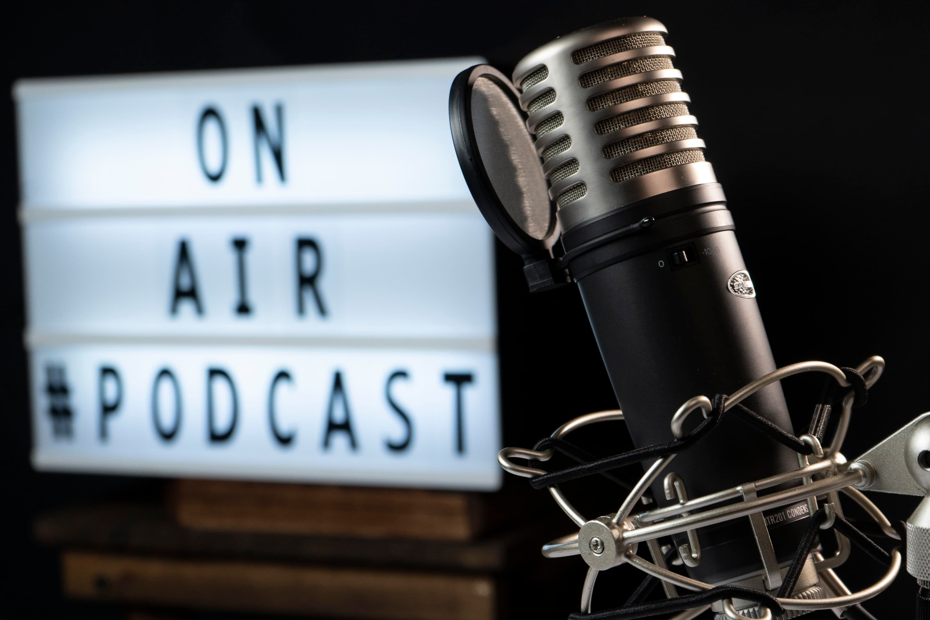 A studio microphone in front of a lightbox that reads ON AIR #PODCAST